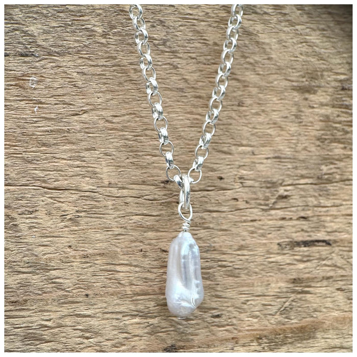 A silver belcher chain necklace with a grey stick pearl, displayed against a wooden background.