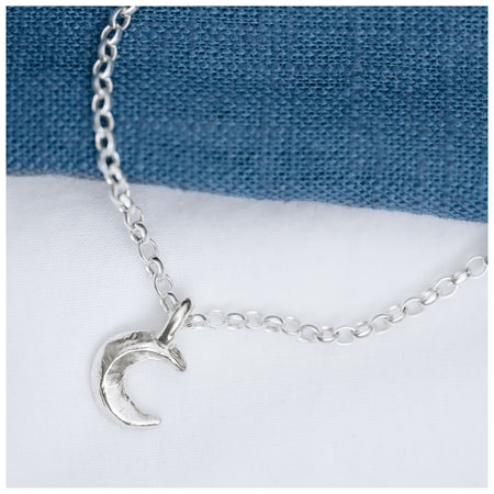 A silver crescent moon pendant on a chain, displayed against a blue textured background.