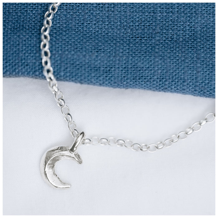 A silver crescent moon pendant on a chain, displayed against a blue textured background.