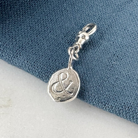 Silver charm with an ampersand on a blue and white background