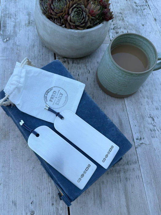 Two silver bookmarks on a blue book with a green mug of tea an a linen bag net to it. 
