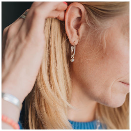 Sterling silver hoop earrings with a  small globe of silver worn by a blonde female.