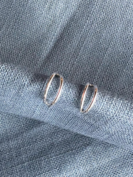 Silver hoop earrings on a textured blue fabric background