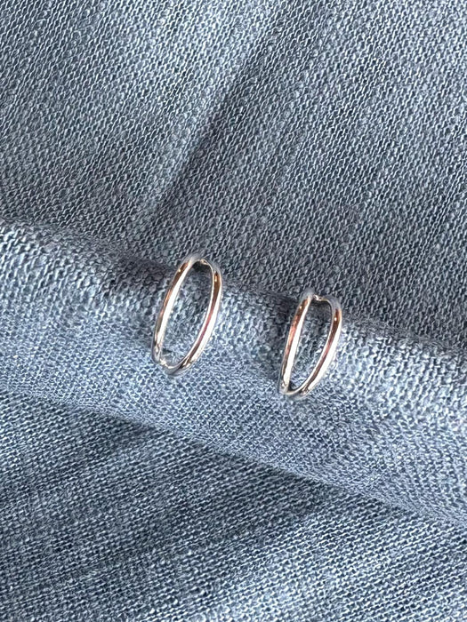 Silver hoop earrings on a textured blue fabric background