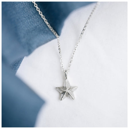 A silver mini guiding star pendant on a chain, displayed against a blue textured background.