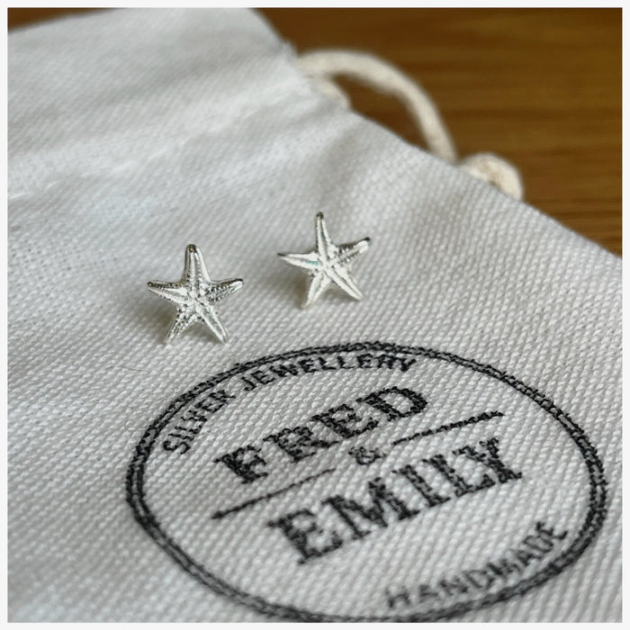 Starfish stud earrings made from sterling silver sitting on a white linen bag