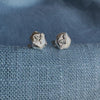 Sterling silver stud earrings with a bee on a piece of silver honeycomb sitting on a blue textured fabric background.