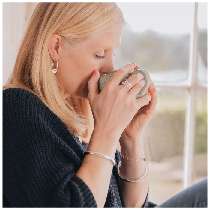 lady drinking coffee out of mug, with silver ring stackers, bracelets and bangles  