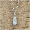 A silver belcher chain necklace with a  white/silver stick pearl displayed against a wooden background.
