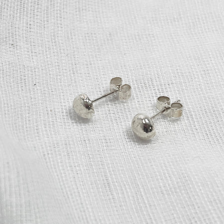 Small Globe studs, made from silver laying on a white linen background