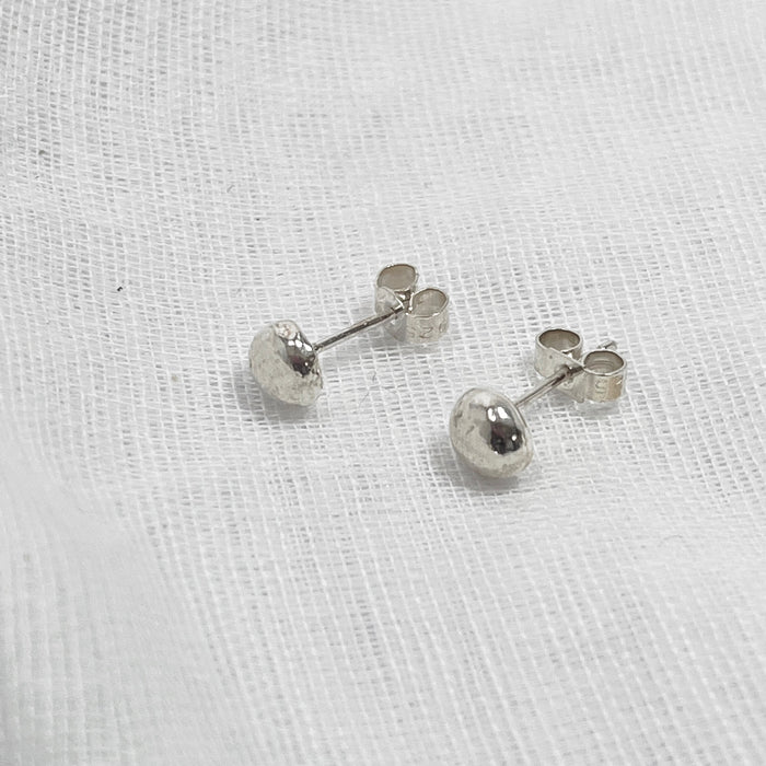 Small Globe studs, made from silver laying on a white linen background