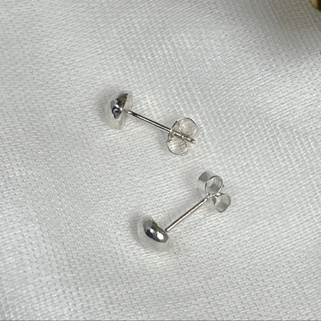 Small Globe studs, made from silver laying on a white linen background